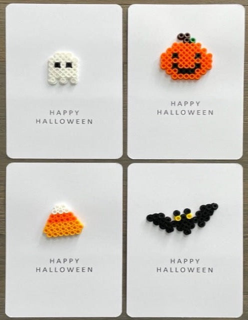 Picture of a set of 4 Happy Halloween cards.  One card is a white ghost, one card is an orange pumpkin with black eyes and smile, one card is a candy corn, and one card is a black bat with yellow eyes. 
