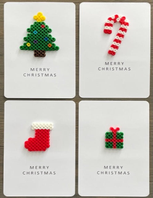 Picture of a set of 4 Merry Christmas cards.  One is a green Christmas tree with dark brown trunk, yellow tree topper, and multi-colored ornaments, one is a red and white candy cane, one is a red stocking with white top, and one is green gift with red ribbon.