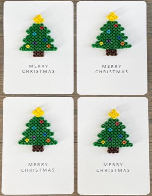 Picture of a set of 4 Merry Christmas cards that each have a green tree with brown trunk, yellow tree topper, and multi-colored ornaments on the cards