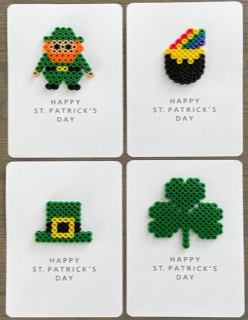 Picture of a set of 4 Happy St. Patrick's Day cards. One has a leprechaun on it, one card has a pot of gold with a rainbow coming out of it, one has a green hat with yellow buckle, one has a green 3 leaf clover on it