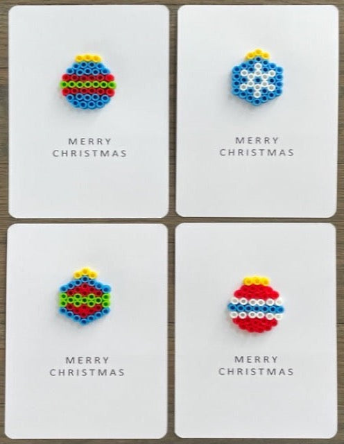 Picture of a set of 4 cards. One is blue ornament with red and lime green stripes, one is blue ornament with white snowflake, one is blue and red ornament with lime green strip, and one is red ornament with white and blue stripes.