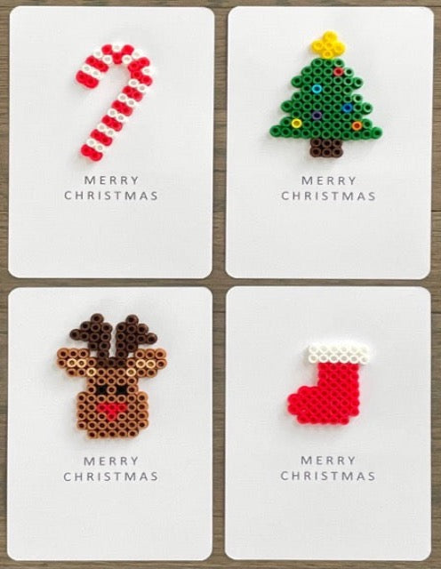 Picture of a set of 4 Merry Christmas cards.  One card is a red and white candy cane, one is a green Christmas tree with dark brown trunk, yellow tree topper and multi-colored ornaments, one is a light brown with dark brown antlers reindeer, and one is a red with white top stocking.