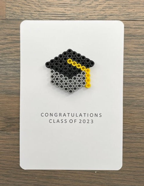 Picture of a Congratulations class of 2023 card that has a light gray and black graduation cap with a yellow tassel on the card