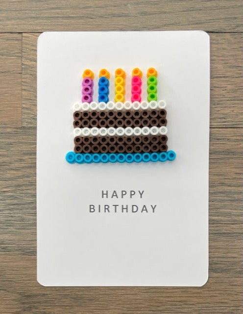 Picture of a Happy Birthday card with chocolate cake with white frosting on a blue tray. Cake has 5 candles on top