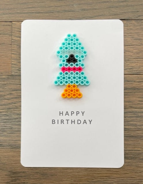 Picture of a Happy Birthday card that has a light blue and pink rocket on it.  Great card for someone who loves space.
