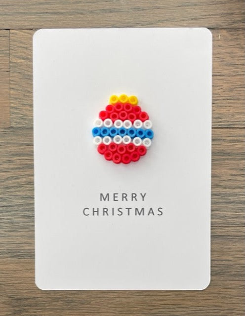 Picture of a Merry Christmas card that has a red ornament with 2 white stripes and 1 blue stripe on it