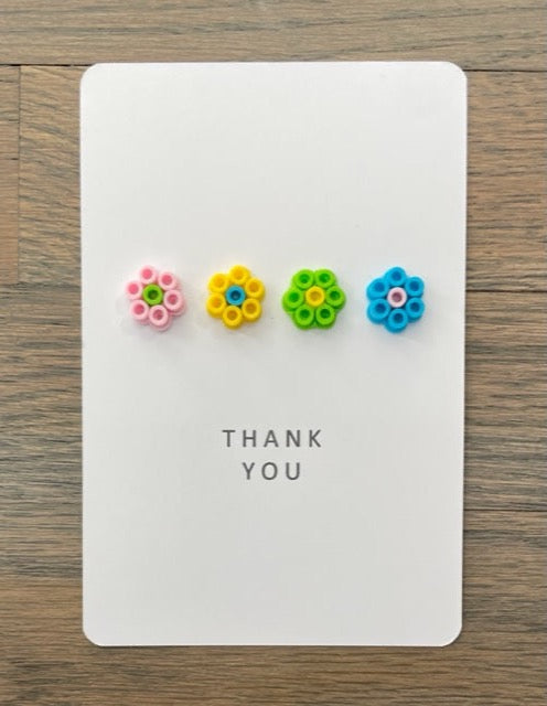 Picture of a Thank you card with 4 flowers across the card.  Flowers are pink, yellow, lime green, and blue
