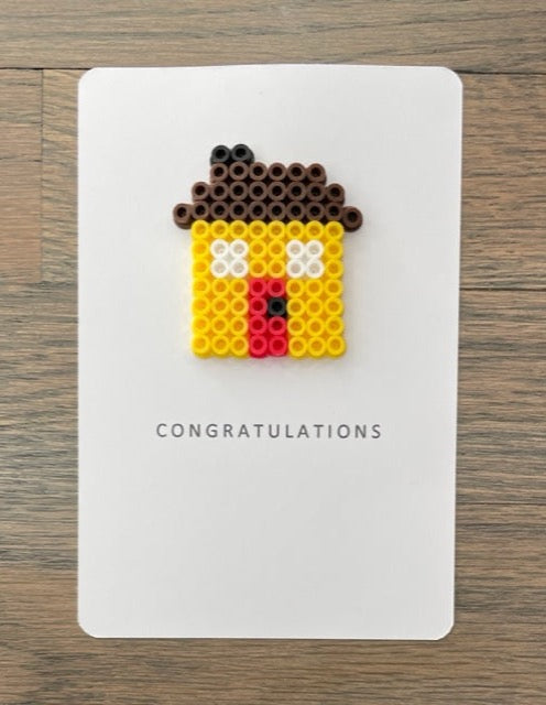 Picture of a congratulations card with a yellow house on it.  House has a red door and dark brown roof