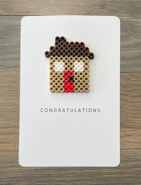 Picture of congratulations card with a tan house on it.  House has a red door and dark brown roof