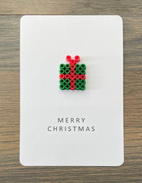 Picture of a Merry Christmas card that has a dark green with red ribbon gift box on it