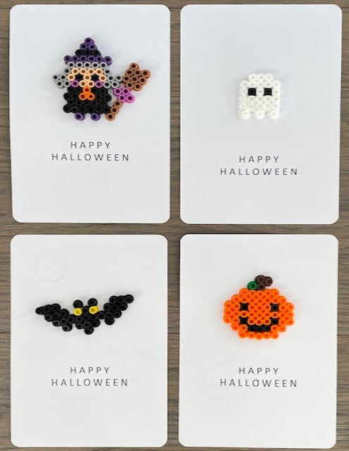 Picture of a set of 4 Happy Halloween cards.  One card is a witch card, one card is a white ghost card, one card is a black bat with yellow eyes, and one card is an orange pumpkin with black eyes and smile card