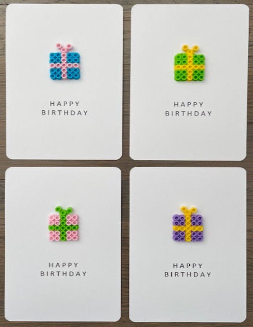 Picture of a set of 4 Happy Birthday cards.  One is blue gift box with pink ribbon, one is lime green gift box with yellow ribbon, one is pink gift box with lime green ribbon, and one is purple with yellow ribbon 