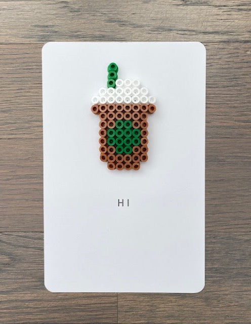 Picture of a card to say Hi that has a light brown, green , and white coffee drink on it